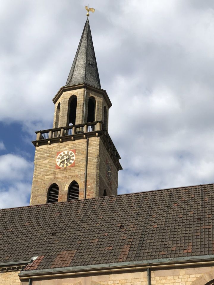 Der Sandsteinturm der Pauluskirche mit Uhr und schiefergedecktem Spitzhelm vor bewölktem Himmel